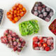 Frozen berries and vegetables in plastic boxes on white wooden background.