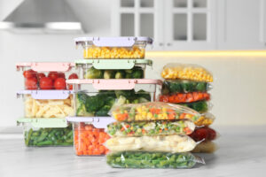 Plastic bags and containers with different frozen vegetables on white marble table in kitchen